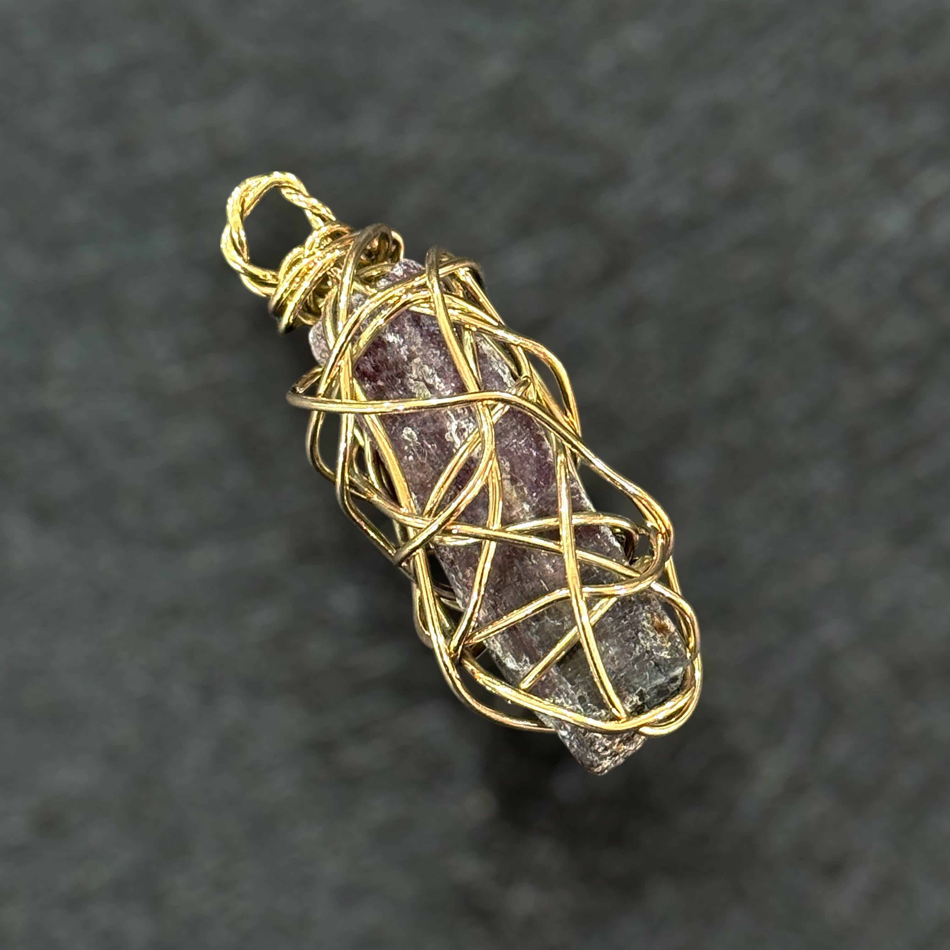 Amethyst crystal pendant wrapped in gold wire on a dark background