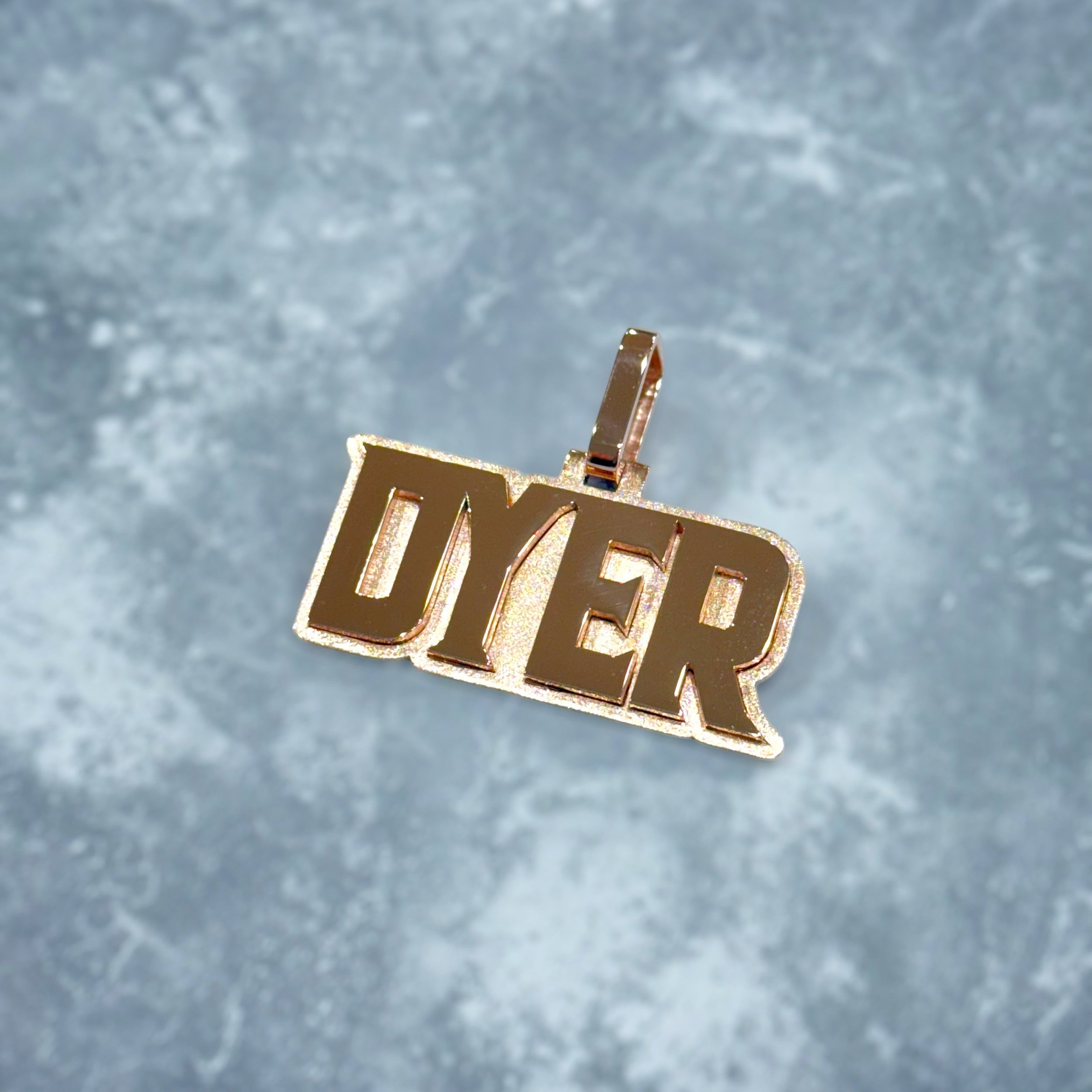 Gold pendant with 'DYER' text on a textured gray background
