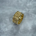 Gold ring with a Greek key design on a gray background